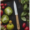 Un Cuchillo Opinel N°113 Dentado reposa sobre una tabla de cortar negra, acompañado de tomates frescos y coloridos y hojas de albahaca. Algunos de los tomates han sido cortados en rodajas para resaltar sus semillas y su interior brillante.