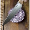 El Cuchillo Opinel N°118 Chef Parallèle, con su hoja afilada y mango de madera, se coloca sobre un repollo morado cortado por la mitad, revelando las intrincadas capas de la verdura sobre una tabla de cortar de madera.