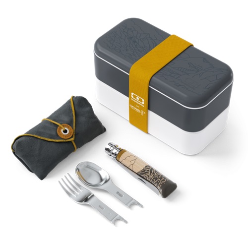 Una lonchera rectangular con tapa gris oscuro y base blanca se mantiene segura con una correa de color amarillo mostaza. Junto a ella se encuentra el Set Opinel para Picnic Monbento de 5 piezas, que incluye un paño gris doblado, un juego de cuchara y tenedor y un cuchillo con mango estampado.