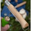 Una imagen detallada del Cuchillo Opinel N°10 Abrebotellas y Sacacorchos muestra su mango de madera parcialmente abierto, dejando al descubierto el sacacorchos de metal en espiral. Se coloca un corcho sobre el sacacorchos, sobre un fondo suavemente enfocado con elementos al aire libre, lo que sugiere una escena de picnic.