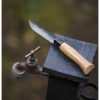 La navaja Opinel N°8 Roble Black, con un elegante mango de madera y una hoja metálica, está elegantemente colocada sobre una superficie de madera oscura. Ubicada junto a un grifo de agua al aire libre, el fondo suavemente difuminado sugiere un ambiente acogedor al aire libre.