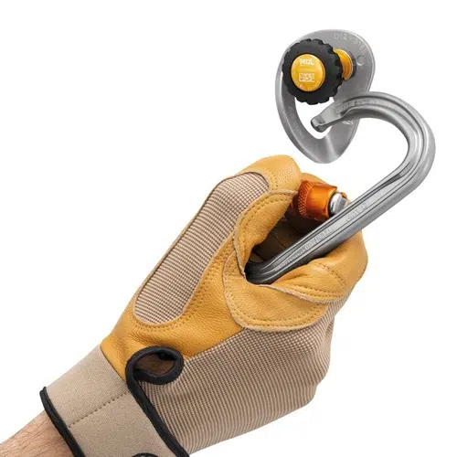 Una persona con guantes de color canela y amarillo sostiene un mosquetón de metal y un anclaje de escalada, mostrando el versátil anclaje móvil Petzl Coeur Pulse de 12 mm. El mosquetón está firmemente sujeto al anclaje, todo sobre un fondo blanco liso.