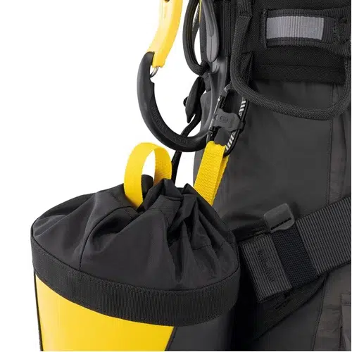 En la imagen de primer plano se puede ver una bolsa de color negro y amarillo, unida a un arnés mediante clips y correas. La bolsa incluye un cierre de cordón, asegurado con una trabilla amarilla, mientras que el arnés cuenta con varias hebillas, cierres y está equipado con el Mosquetón Auxiliar Petzl Mino para una mayor seguridad.