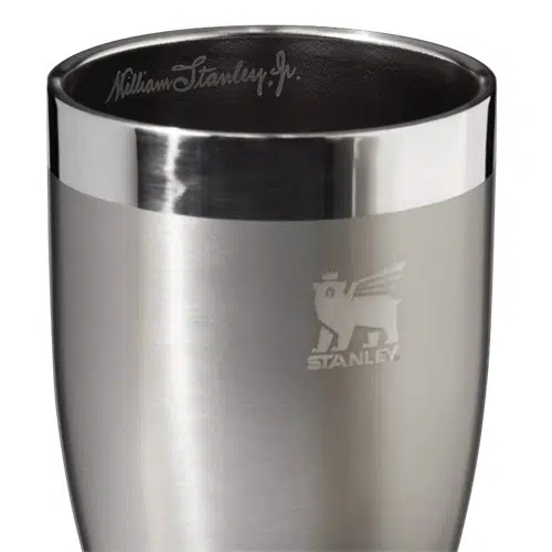 El Vaso Stanley The Golden Hour Prismatic™ 443ml es una taza de acero inoxidable adornada con un borde superior brillante grabado con "William Stanley Jr." y una representación en relieve de un oso con alas y una corona, junto con la palabra "Stanley" en el costado.