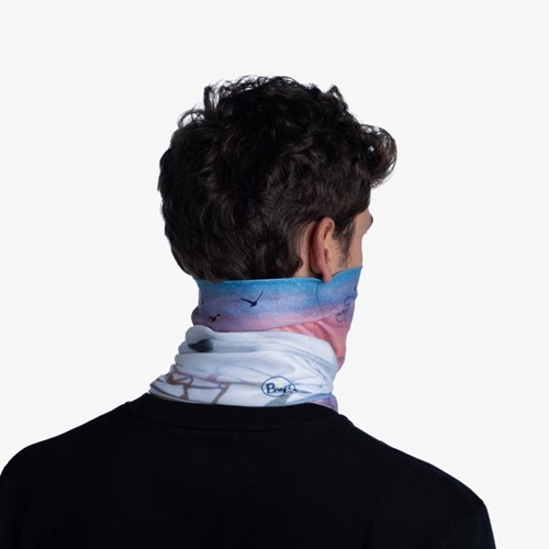 Desde atrás, una persona con cabello castaño rizado lleva puesta la bandana Buff ThermoNet White Ocean, que luce un estampado de cielo y pájaros en tonos pastel. Le cubre parcialmente el cuello y la parte inferior del rostro y se combina a la perfección con una camiseta negra.