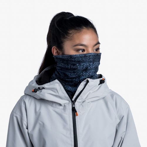 Una persona vestida con una chaqueta gris claro con un cierre naranja lleva una polaina para el cuello Bandana Buff Original EcoStretch Haiku Dark Navy sobre la boca y la nariz. Con el pelo largo atado hacia atrás, mira hacia un lado y derrocha estilo desenfadado.