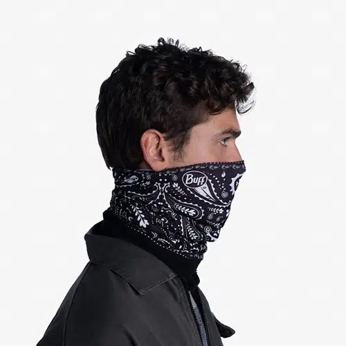 Una persona con cabello rizado lleva una polaina para el cuello con estampado blanco y negro de la colección EcoStretch que le cubre la mitad inferior del rostro. Está vestida con una chaqueta oscura y se encuentra de perfil sobre un fondo liso.