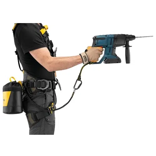 Ataviada con equipo de seguridad, como un arnés y guantes, una persona utiliza un taladro eléctrico mientras está sujeta de forma segura con el cordón de seguridad Cabo Porta Herramientas Petzl Tooleash. El cordón se conecta a una bolsa de herramientas y la imagen resalta la parte superior del cuerpo y el conjunto de herramientas contra un fondo blanco.