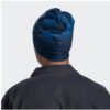 En la imagen se ve a una persona de espaldas, vestida con una chaqueta oscura y un gorro Buff ThermoNet S-Wave Blue adornado con patrones abstractos. El fondo es liso y de color claro.