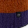 Primer plano de un gorro de mezclilla Buff Tricot Nilah con parte superior naranja y parte inferior violeta. Se ve una pequeña etiqueta negra que dice "Buff" en el borde.
