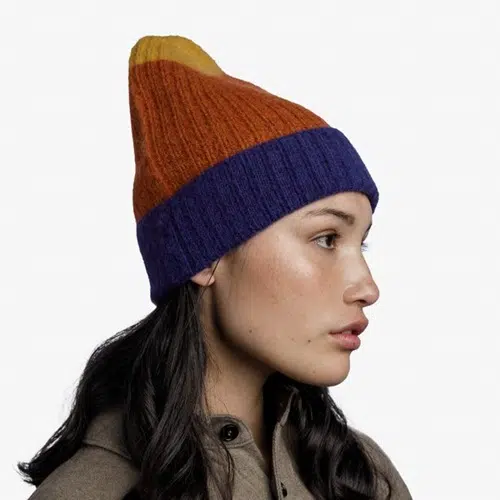 Una mujer de perfil lleva un gorro de mezclilla de punto Gorro Buff Tricot Nilah, con detalles en naranja, amarillo y azul. Su pelo largo y oscuro cae en cascada sobre su abrigo marrón sobre un fondo liso.