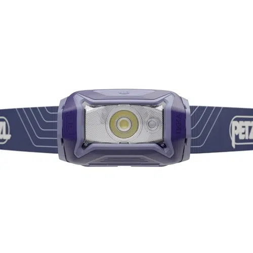 La linterna frontal Petzl Tikka 350lm viene en color violeta y cuenta con una luz LED principal acompañada de dos luces más pequeñas. Proporciona 350 lúmenes de brillo e incluye una correa azul ajustable con patrones blancos, en la que se destaca el nombre de la marca "Petzl".