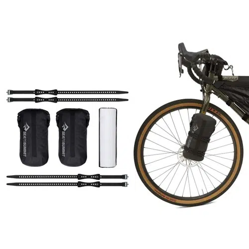 Junto a la bicicleta Carpa Sea To Summit Alto TR2 Bikepack para dos personas se encuentra una bicicleta equipada con una bolsa delantera en la horquilla. Junto a ella hay dos bolsas negras, un cilindro blanco y cuatro correas negras ajustables diseñadas para un montaje seguro, componentes cruciales del equipamiento para bikepacking.