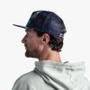 Un hombre con una sudadera con capucha gris claro está de perfil sobre un fondo liso y lleva una gorra Jockey Buff Trucker Kingara Night Bluel, con visera plana y diseño de malla. Su cabello castaño corto se asoma a través de la gorra mientras mira hacia la izquierda.