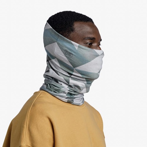 Una persona viste un suéter amarillo con un Bandana Buff Original EcoStrech Lidre Multi con patrones geométricos grises levantado sobre su nariz y boca, de pie sobre un fondo blanco liso.