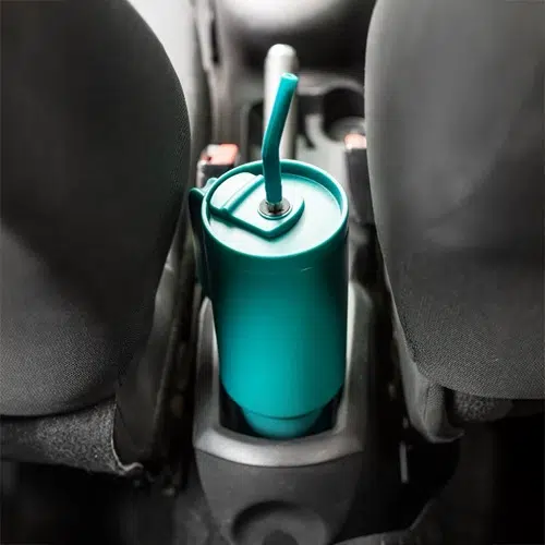 Un Vaso Térmico Quencher Halten 1.2L en color verde azulado, completo con una pajita, se coloca en el portavasos entre dos asientos del automóvil.