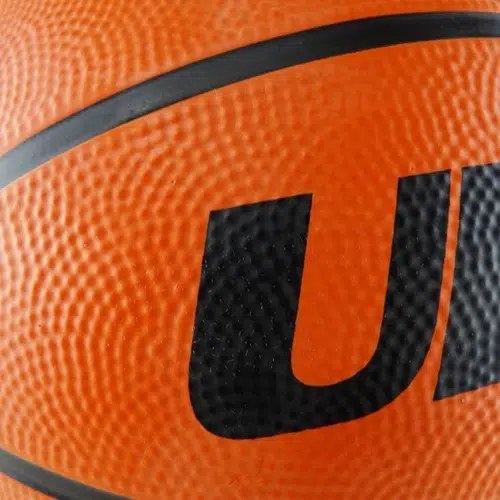 Primer plano de un Balón de Básquetbol Uk Time Sport BRX7 N°7 en color naranja, con una superficie texturizada con letras negras parcialmente visibles. La imagen enfatiza la textura granulada del balón y muestra parte de su intrincado diseño.