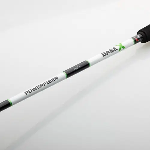 Primer plano de una caña de pescar blanca y negra con las palabras "POWERFIBER" y "Caña Dam Base X Spin" impresas en letras verdes. El elegante mango muestra el diseño de Caña Dam, mientras que la caña está colocada en diagonal sobre un fondo blanco liso, lo que representa la precisión de la ingeniería de Base X Spin.