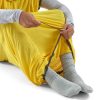 Una persona está sentada en el suelo, con calcetines grises y un forro amarillo brillante de la marca Sea To Summit Reactor Mummy Standard. Tira de un cordón en el dobladillo, creando un espacio cerrado alrededor de sus piernas. Este forro versátil también cubre sus brazos, que son parcialmente visibles.