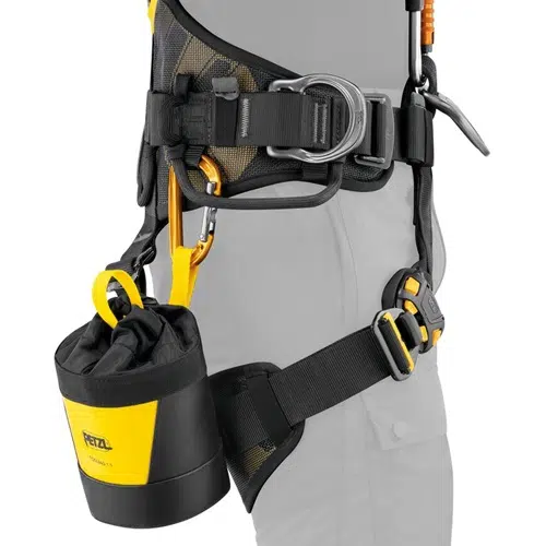 Primer plano de un arnés de seguridad que muestra la Bolsa Portaherramientas Petzl Toolbag 1.5 en amarillo y negro vibrantes, convenientemente sujeta al costado con un mosquetón. El arnés cuenta con múltiples correas y hebillas, diseñadas por expertos para escalar con seguridad o con fines de seguridad.