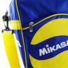 Primer plano del Bolso Portabalones Vóleibol MIKASA V200W, un bolso deportivo de color azul y amarillo que muestra su logotipo de forma destacada. El bolsillo frontal, parcialmente visible, incluye una cremallera y el bolso está equipado con una correa amarilla para el hombro para llevarlo cómodamente.