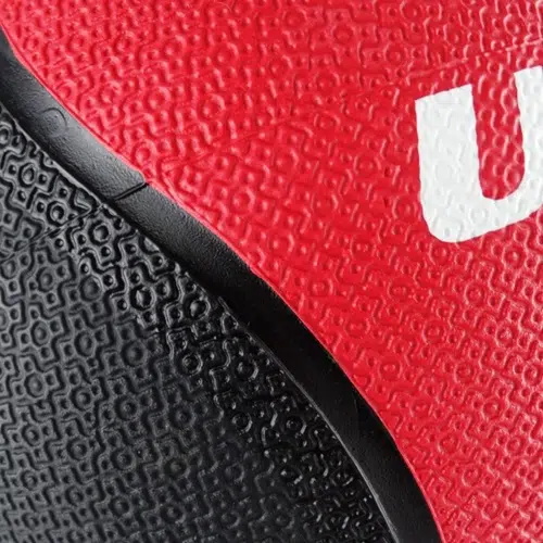Primer plano de una superficie texturizada de color rojo y negro que recuerda a la que se encuentra en el Balón Medicinal con Rebote de 1 kg. Presenta una porción de una "U" blanca en medio de patrones de granulados visibles típicos de los balones de baloncesto.