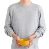 Una persona con una sudadera gris sostiene un cuenco amarillo Passage Bowl con ambas manos sobre un fondo blanco. El cuenco redondo tiene una superficie texturizada que le aporta profundidad a su tono vibrante. La imagen se centra únicamente en el cuenco, lo que lo convierte en la pieza central de este sereno momento de Sea to Summit.