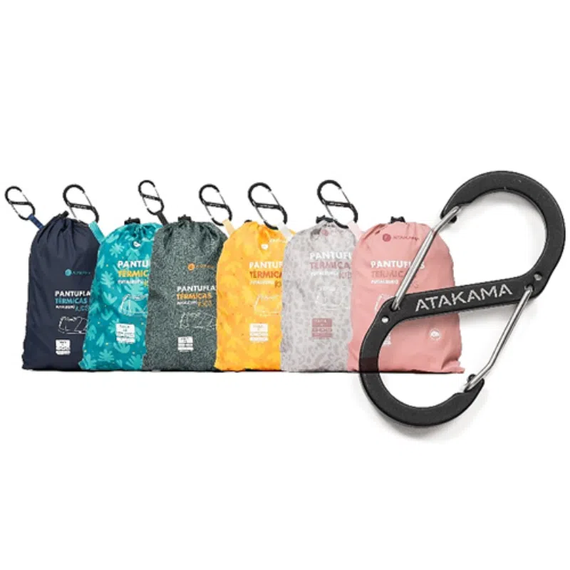 Dos filas de vibrantes bolsas Pantuflas Térmicas Atakama Outdoor Futaleufú Kids Nu-B Foam vienen con mosquetones adjuntos. Cada bolsa está adornada con gráficos y textos divertidos, diseñados para las aventuras de Atakama Outdoor. Un prominente mosquetón negro con el logotipo de "Atakama" se muestra en el lado derecho de la imagen, ideal para expediciones a Futaleufú o viajes infantiles.