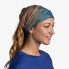 Una persona que lleva un Bandana Buff CoolNet UV Sanve Multi sonríe de perfil sobre un fondo blanco liso; su camisa azul añade un toque de color a la serena escena.