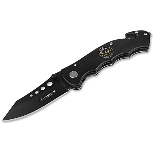 Navaja de bolsillo plegable negra con hoja parcialmente dentada. El mango presenta un botón plateado y un emblema circular con elementos náuticos. Las palabras "Navaja Boker Magnum Us Navy Seals 01MB856" están impresas en la hoja y el mango, respectivamente.