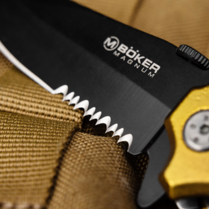 Primer plano de un cuchillo Navaja Magnum Army Rescue 01LL471 con una hoja negra parcialmente dentada. Colocado sobre una tela marrón texturizada, la imagen revela un atisbo del mango dorado en el lado derecho.