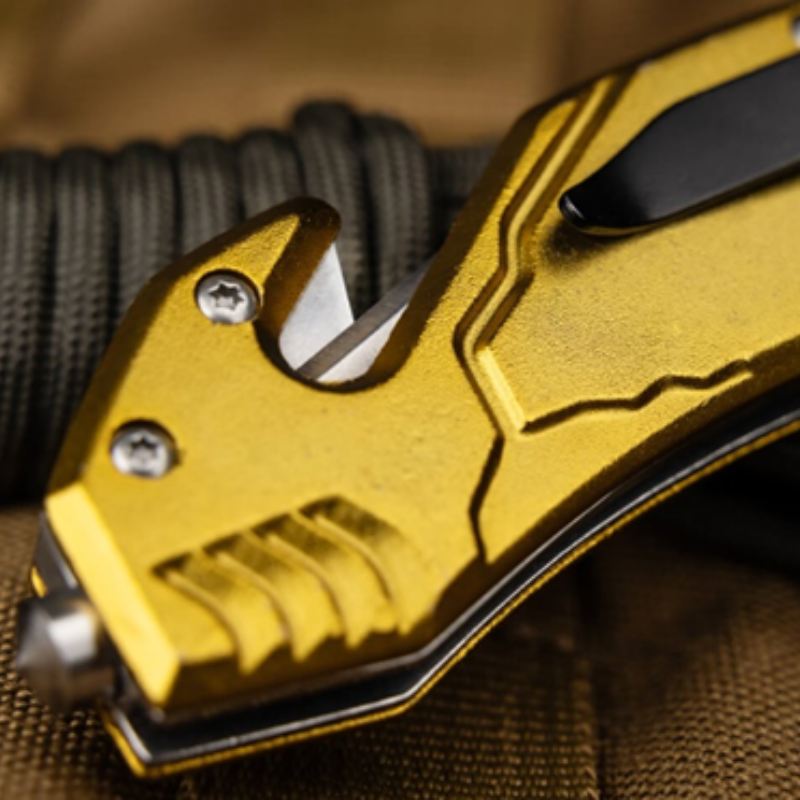 Primer plano de una Navaja Magnum Army Rescue 01LL471 con la hoja parcialmente expuesta y el clip negro. La carcasa metálica de la navaja, con patrones texturizados, brilla contra el fondo borroso.