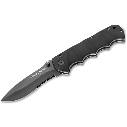 Navaja Boker Magnum Black Spear 01RY247, de color negro, con hoja parcialmente dentada. El mango ergonómico tiene ranuras para los dedos y una pequeña anilla de metal en el extremo. La hoja muestra el logotipo "Magnum by Böker" y cuenta con un botón para el pulgar para facilitar su apertura.