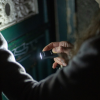 Una persona sostiene una Linterna Llavero Led Lenser K6R 400lm 502577 que ilumina una puerta cerrada en un área con poca luz. Está ajustando su agarre en la cerradura, lo que sugiere que podría estar abriéndola o examinándola de cerca.