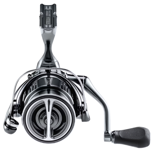 Primer plano de la vista frontal del carrete de pesca Shimano Stella FK. El carrete presenta un elegante acabado metálico que muestra componentes como la manivela, el carrete y el brazo de agarre.