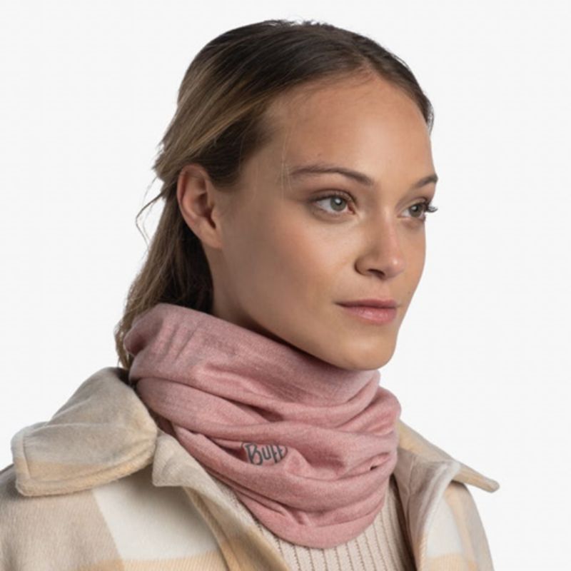 Una mujer que lleva una polaina para el cuello Bandana Buff Merino Midweight Melange Rosewood y un abrigo a cuadros beige y blanco mira hacia un lado. Tiene el pelo castaño claro recogido hacia atrás y una expresión neutra sobre un fondo liso, lo que exuda un aire de elegancia discreta.