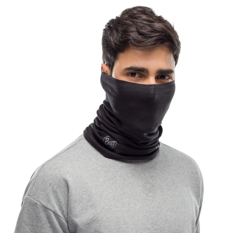 Una persona con una camisa gris lleva una polaina Bandana Buff ThermoNet Solid Black sobre la nariz y la boca, con el logotipo "Buff" visible contra el fondo blanco liso.