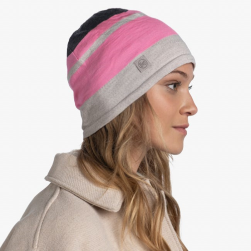 Perfil de una persona que viste un gorro Buff Merino Move rosa y gris combinado con un abrigo beige, sobre un fondo blanco liso.