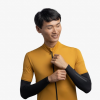 Una persona que viste una camiseta ciclista amarilla sobre la marca Manguitos para Brazos Buff sonríe y ajusta la cremallera, sobre un fondo blanco liso.