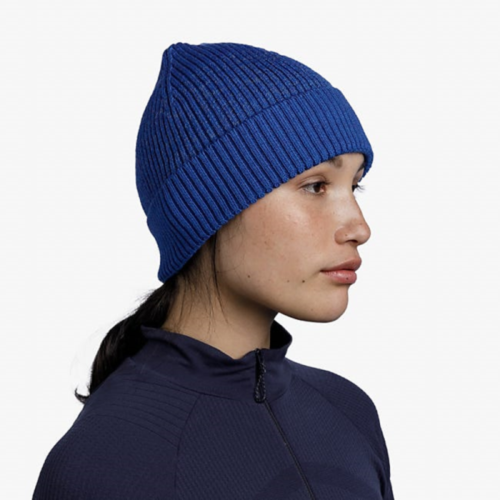 Perfil de una persona que viste un gorro Buff Merino Active Solid Cobalt combinado con una chaqueta oscura con cremallera, sobre un fondo blanco liso.