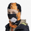 Una persona se pone una Pasamontañas Buff ThermoNet Niños Vem Multi, con un estampado naranja y negro y una cubierta facial a juego. Debajo de una chaqueta oscura, lleva una sudadera con capucha beige, todo sobre un fondo blanco liso.