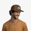 Hombre sonriendo y usando la gorra Jockey Buff Explore Trucker Rhoes Brown, mostrando la combinación de colores marrón y detalles de la malla trasera.
