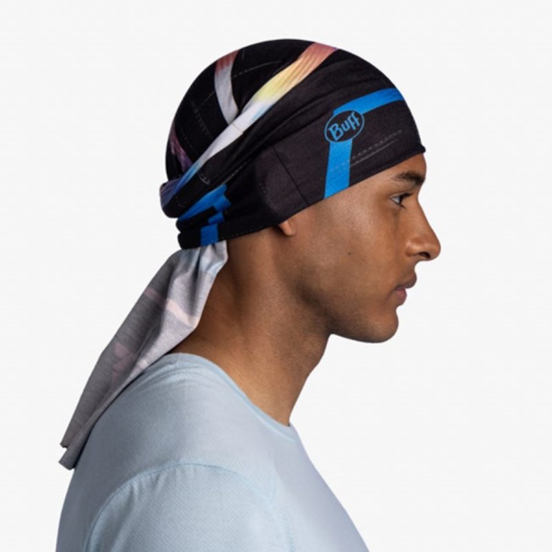 Una persona que lleva un pañuelo para la cabeza Bandana Buff CoolNet UV Reflectante Matsy Multi con un diseño azul y negro en el costado está mirando hacia la derecha, luciendo una camisa azul claro sobre un fondo claro y liso.
