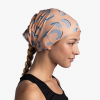 Una mujer con un peinado trenzado lleva la bandana Buff CoolNet UV Reflectante Thisy Multi, que muestra un diseño de formas de medialuna azules sobre un fondo melocotón. Aparece de perfil, mirando hacia la derecha, y lleva una camiseta negra sin mangas sobre un fondo sin adornos.
