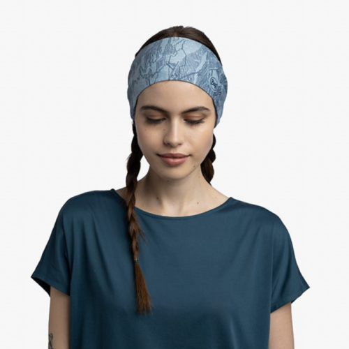 Una persona que lleva una elegante diadema Cinta Buff CoolNet UV Wide Laven Mist y una camisa verde azulado se encuentra sobre un fondo blanco liso, con los ojos cerrados y el cabello peinado en dos trenzas.