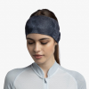 Una persona con cabello largo, que lleva una cinta para la cabeza Cinta Buff CoolNet UV Wide en color grafito Bonsy, mira hacia abajo con expresión neutra. Su camiseta deportiva azul claro con cremallera contrasta sutilmente con el fondo liso.