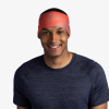 Una persona sonríe mientras usa una diadema Cinta Buff CoolNet UV Wide Arthy Nectarine con un logotipo y una camiseta azul marino sobre un fondo blanco liso.