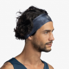 Un hombre con cabello ondulado viste una diadema Cinta Buff Fastwick Bonsy Graphite oscura y una camisa azul sin mangas, mirando hacia un lado contra un fondo liso.