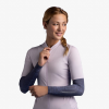 Una persona que viste una camiseta de ciclismo violeta claro y mangas de brazo Buff está de pie sobre un fondo liso, mirando hacia su derecha con una leve sonrisa. Lleva el pelo recogido en una trenza sobre un hombro.