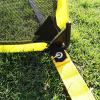 Primer plano de una esquina de la Mini Cancha Fútbol Train Plegable. La portería cuenta con una tela amarilla resistente y una red negra, equipada con ojales de metal y una correa amarilla para asegurarla al suelo sobre un campo de césped, lo que la hace perfecta para entrenar en tu propia mini cancha.